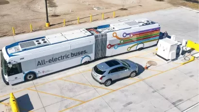 Aerial view of electric bus parked next to silver SUV in parking lot in Austin, Texas. Bus says "All eelctric buses" on side.