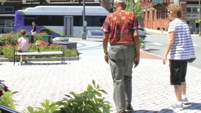 Two people walking away from camera through pedestrian plaza in street in Richmond, Virginia with purple and white city bus moving in background.