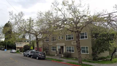 Two-story green apartment building in residential neighborhood in Berkeley, California with tall street trees.