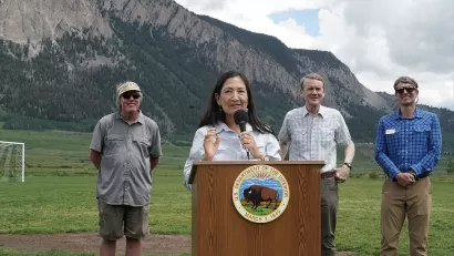 Sec. Deb Haaland speaking at dais outdoors with Colorado mountains in background and three officials standing behind her announcing protection of Thompson Divide.
