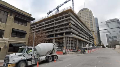 Construction on a high-rise, with cement trucks and tall cranes, is visible on an Austin Street.