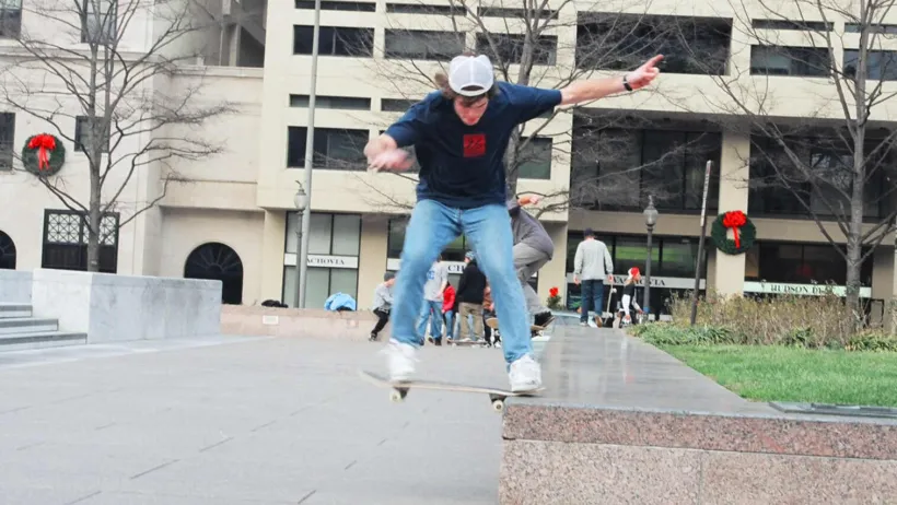 Boy wearing jeans and white cap skateboards off marble ledge in Freedom Park, Washington DC.