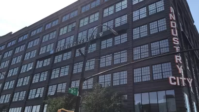 Looking up at black multi-story building with Industry City neon sign on corner.