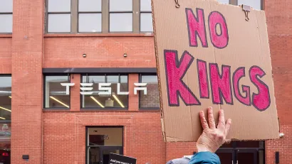 Close-up on cardboard sign reading 'No Kings' being held up at protest at Tesla offices in Brooklyn, New York.