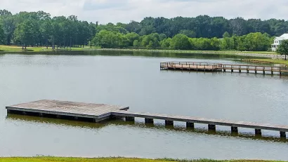 View of docks on lake surrounded by green trees and lawns with one white house at right