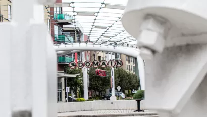 A picture of a decorative sign announcing “The Domain” surrounded by high density shops and apartments.