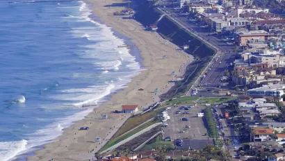 A parking lots and homes sit on a bluff above a large beach on Pacific coast in Southern California.