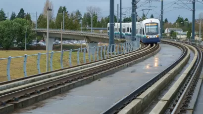 A Link light rail transit train navigates a corner with an empty field and parked cars in the background.