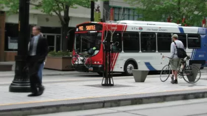 White, red, and blue Utah Transit Authority bus at stop with man standing on sidewalk next to bicycle