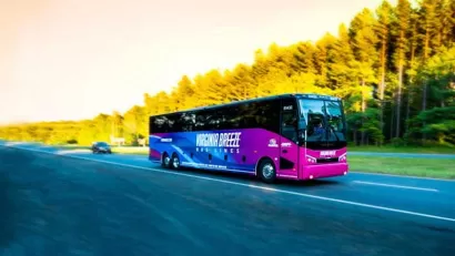 Purple Virginia Breeze intercity bus driving down blurred road with trees on roadside.