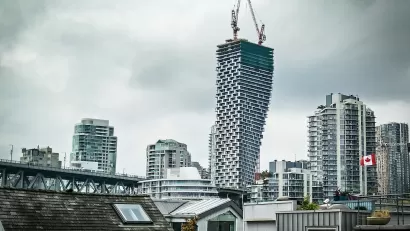 View of Vancouver House skycraper under construction with two cranes at top and other downtown Vancouver buildings surrounding it against a grey sky