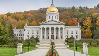 A picture of the Vermont State Capitol building with fall colors on display on trees in the background.