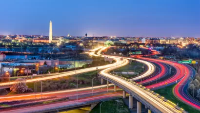 An image of Washington D.C. with highways and the streaks from car head and tail lights in the foreground, and the Washington Monument in the background.