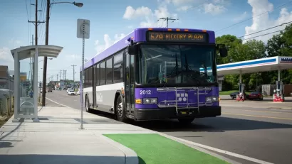 Purple buss pulls up to bus stop in green bus lane.