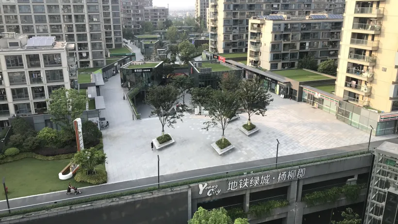 Complex of high-rise apartment buildings around a concrete plaza with several large trees in China.