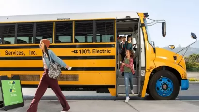 Yellow electric school bus with preteen students exiting.