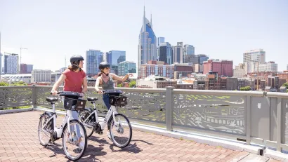 Two people on Nashville BCycle bike share wearing helmets loking out over railing at downtown skyline.