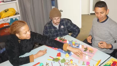 Three people gather around a table to discuss maps made of toys and found objects.