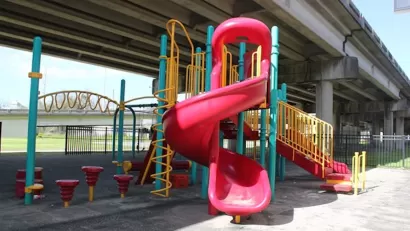 Red, yellow, and green plastic playground equipment in small park under Claiborne Expressway overpass in New Orleans, Louisiana.