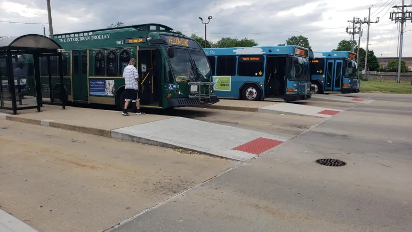 Three green and teal buses at a multi-lane bus station.