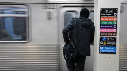 View from back of person in black clothes and hat waiting to board train at Chicago train station with blurry train in front of them.
