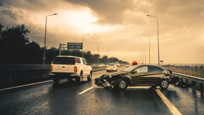 Small black car with mangled bumper sitting sideways on an asphalt road