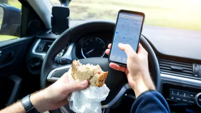 Close-up of person eating sandwich and texting while driving