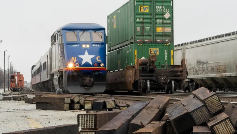 Dark blue Amtrak train passing green shipping containers on freight train in Greensboro, North Carolina.