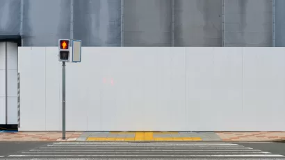 Crosswalk leading to sidewalk and blank construction wall with pedestrian crossing light