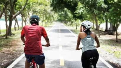Two people riding bikes with helmets on paved park trail