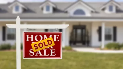 For sale sign with SOLD sign pasted over it in front of white suburban house