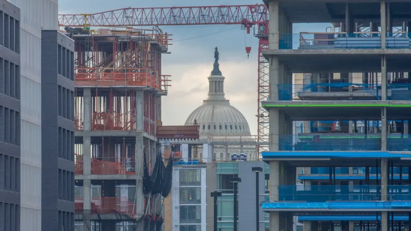 View of neoclassical dome with statue on top through construction of high-rise buildings in Washington DC.