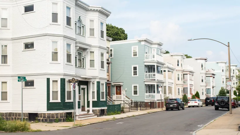 Corner of block with light-colored three-story wooden apartment buildings in Boston, Massachusetts.