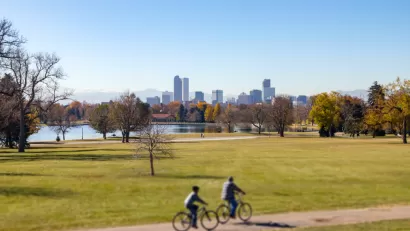 Two bike riders on trail in part with Denver, Colorado skyline in background