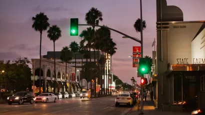 View of Culver City street with stoplights, white cars, and palm trees sillhouetted against a purple sunset sky