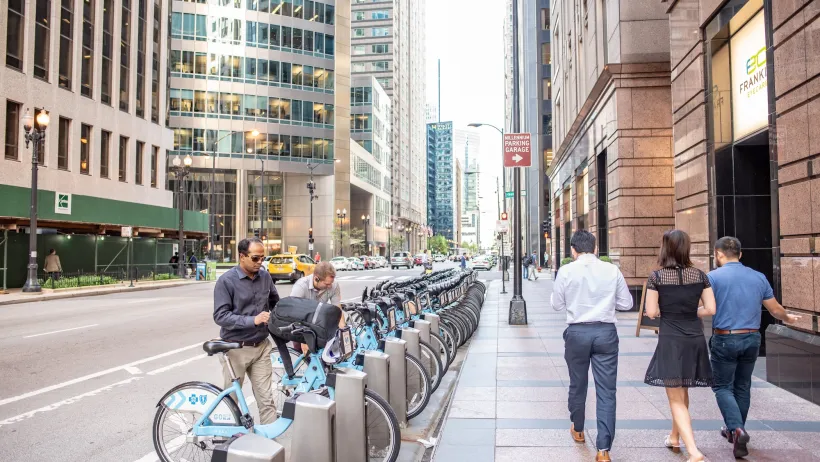 Divvy bike share station in Chicago with people checking out blue bikes.