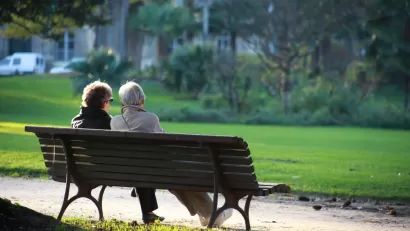 View from back of two elderly people sitting on park bench
