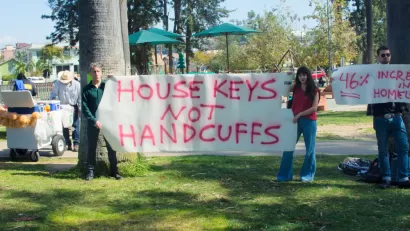 Two people holding sign that says "house keys not handcuffs" during an anti-homelessness event in Los Angeles, California
