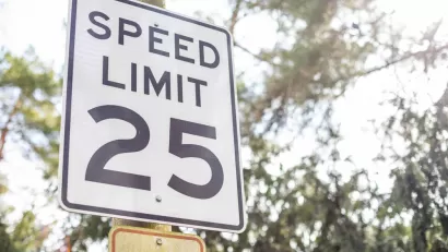 Black and white 25 mph speed limit sign on post with trees in background