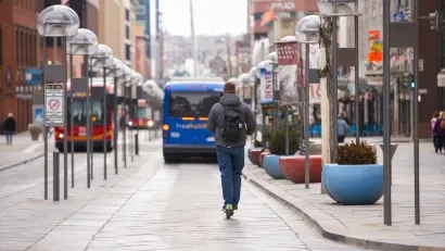 Man rides green share scooter on protected bus lane with blue bus in front of him in Denver, Colorado.