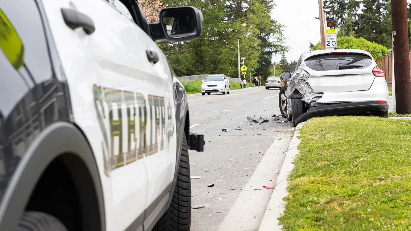Close-up on Sheriff car parked next to grassy curb with silver car with damaged bumper stopped on grass immediately after crash.