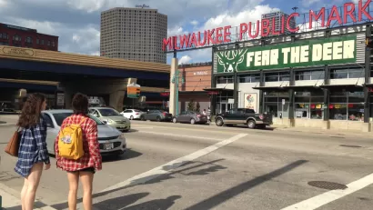 Two women waiting to cross street facing Milwaukee Public Market sign