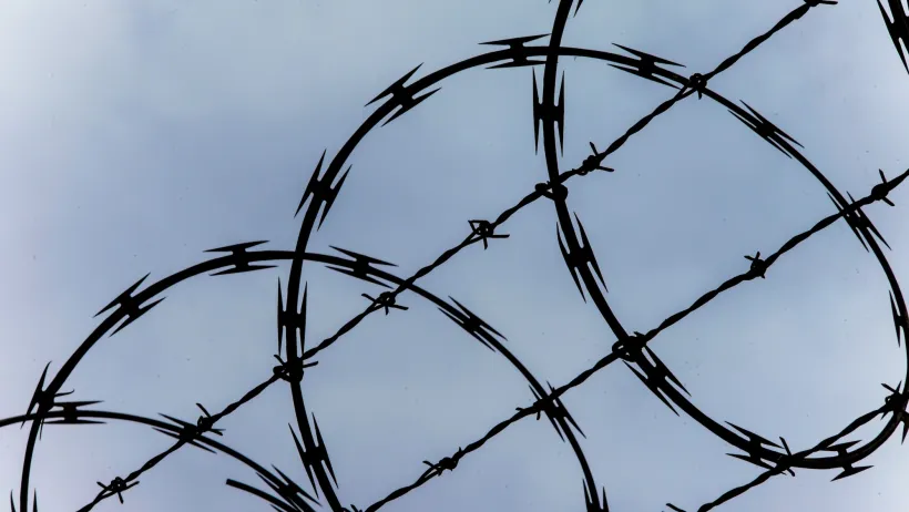 Close-up of razor wire at top of fence against blue sky.