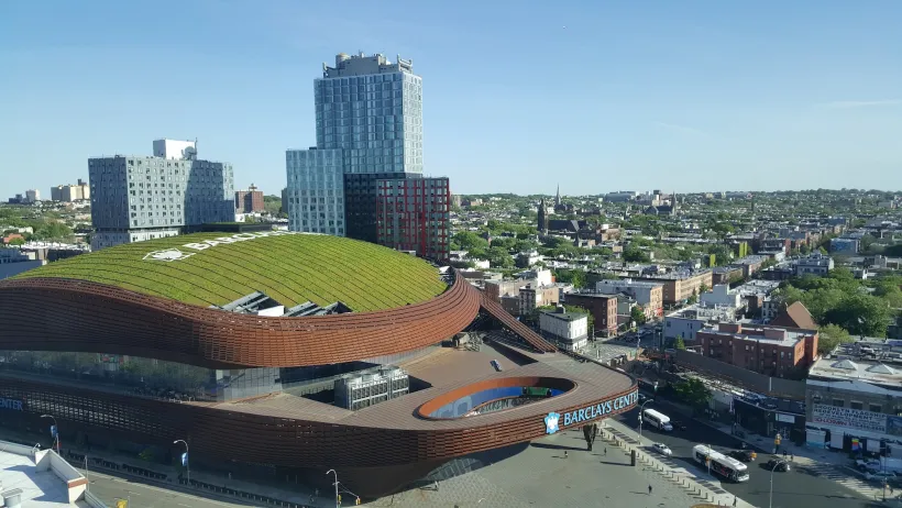 Aerial of Barclays Center stadium in New York Coty with green roof and modern towers behind it.