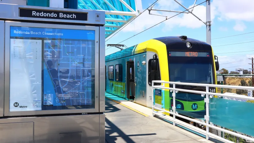Yellow and black Los Angeles Metro light rail train stopped at Redondo Beach elevated outdoor station.