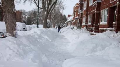 Snow-covered Chicago sidewalk with piles of snow on either side and red brick homes on the right