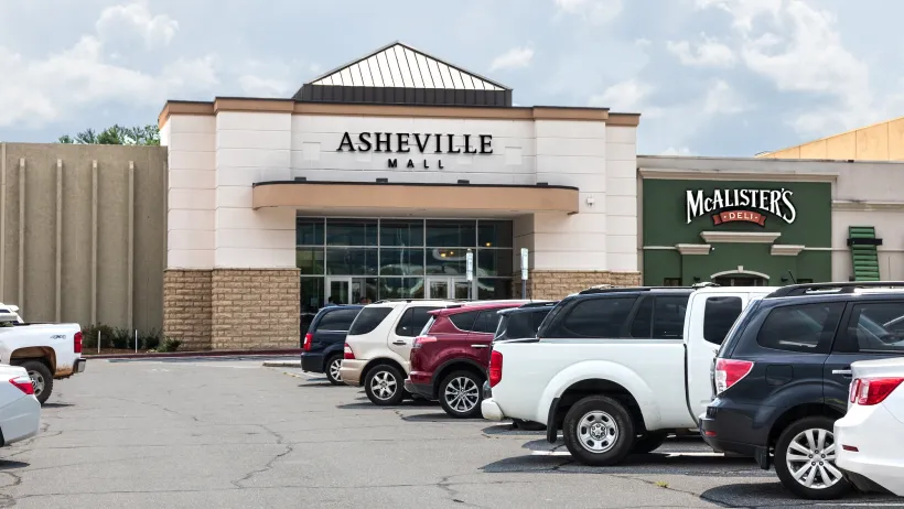The main front entrance to the Asheville Mall, showing parking lot and cars.