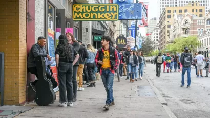 Austin's Sixth Street full of pedestrians during SXSW festival with yellow sign for Chuggin Monkey bar in foreground