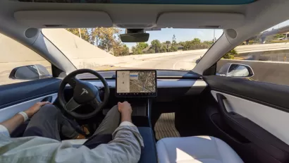 Interior of Tesla car with driver holding hands off wheel in 'full self-driving' mode