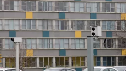 Two white traffic enforcement cameras above a road in Ottawa, Canada with a colorful multistory building in background